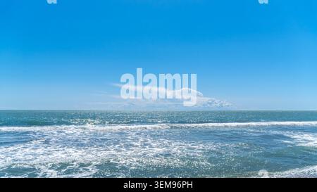 Wide sea horizon with blue water and white breaking waves under a clear sky with a large white cloud. Minimalist coastal landscape in Dalaman, Turkey. Stock Photo