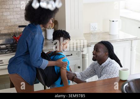 African American family adjusting child's backpack on kitchen counter while woman in denim shirt Stock Photo