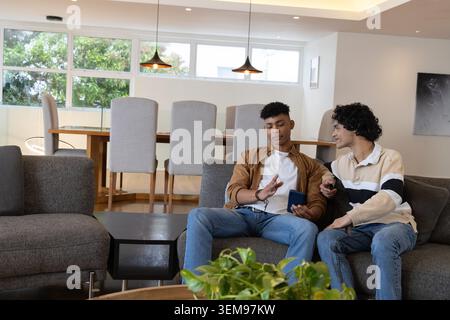 Two men sitting on right side of gray sectional sofa in modern living room holding smartphone Stock Photo