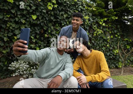 Teenage male friends taking selfie in backyard on concrete ledge holding smartphone and soccer ball Stock Photo