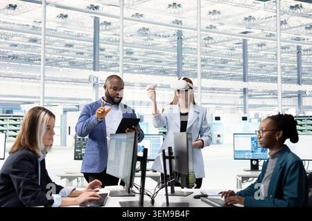 Multiracial team testing microchip electronics prototypes using VR, brainstorming. Teamworking colleagues using virtual reality goggles to upgrade industrial hardware in semiconductors RD laboratory Stock Photo
