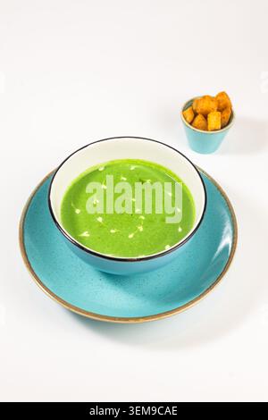 High angle shot of a vibrant green spinach puree soup featuring elegant cream heart patterns, presented in a blue bowl with crispy croutons Stock Photo