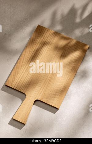 High-angle minimalist background featuring a blank wooden cutting board on a rustic countryside kitchen table. Captured in a warm, pastel color palett Stock Photo