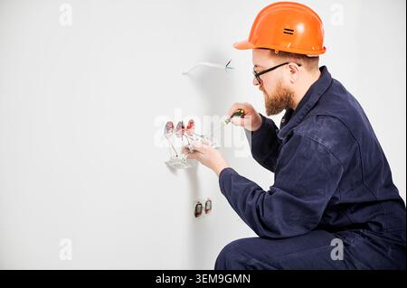 Electrician connecting wall sockets with screwdriver and exposed wiring. Indoor installation process with electrical cables, power system setup and home renovation concept Stock Photo
