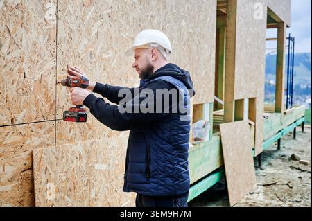 Construction worker fastening sheathing boards to timber structure using power tool, symbolizing home building process, structural development and professional craftsmanship Stock Photo