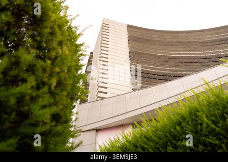 Modern architectural building showcasing curved elements and sharp angles contrasted with green foliage Stock Photo