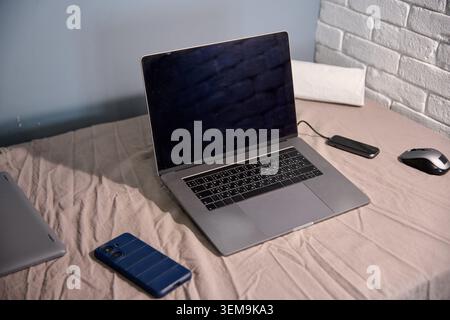 Dark laptop with black keyboard rests open on beige blanket in light room corner featuring light gray brick wall and blue wall, accompanied by blue sm Stock Photo