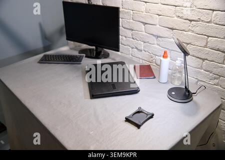 Neat modern desk setup featuring black computer monitor and keyboard, closed black laptop, small red notebook, bottle of glue, hand sanitizer, and com Stock Photo