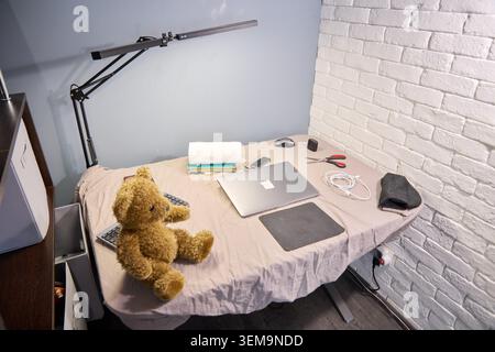 Neat workstation featuring laptop mouse pad and charging cables arranged on cloth covered desk opposite white brick textured wall and modern black adj Stock Photo