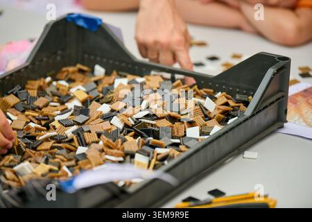 Numerous rectangular puzzle pieces in shades of brown, black, and white scattered on grey plastic sorting tray on white surface. Partial hands pointin Stock Photo
