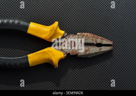 Rusty Pliers with Yellow Handle on Dark Background Stock Photo