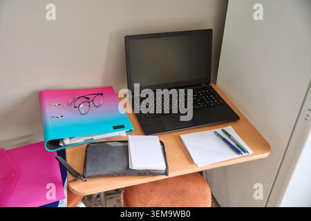 Minimalist wooden desk setup with black laptop opened beside gradient pink blue notebook and writing instruments against plain white walls. Soft natur Stock Photo