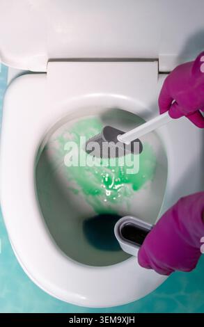 A vivid top view shot showing a person cleaning a toilet bowl sprayed with green liquid detergent using a modern silicone brush. Stock Photo