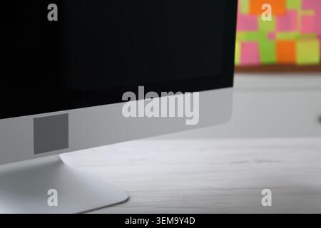 Computer on light wooden table and board with colorful sticky notes indoors, selective focus. Multitasking and deadline Stock Photo