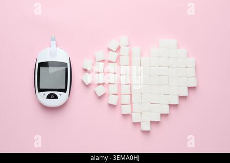 Diabetes. Digital glucometer and heart made of sugar cubes on pink background, flat lay Stock Photo