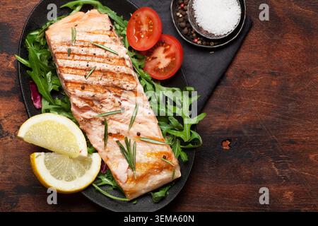 Grilled salmon fish fillet with salt, pepper and rosemary over salad leaves. On wooden table. Top view flat lay with copy space Stock Photo