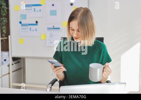 Happy female entrepreneur using smart phone in office. Stock Photo