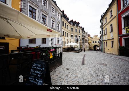 Lublin, Poland - May 13, 2026: Empty cobblestone street in Lublin old town lined with pastel buildings, outdoor cafes and an arched gateway. Stock Photo