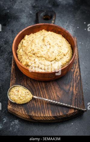 German Bavarian sweet mustard condiment closeup showing thick grainy texture in wooden bowl on black background. Stock Photo