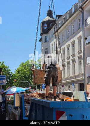 Construction Worker Emptying Debris into Truck – A construction worker carefully guides a hanging bucket of debris from a building site, directing it Stock Photo