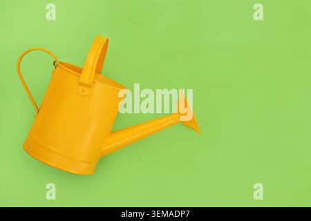 Yellow metal watering can for indoor or outdoor and patio gardening. Classic garden lightweight tool design on green background. Stock Photo