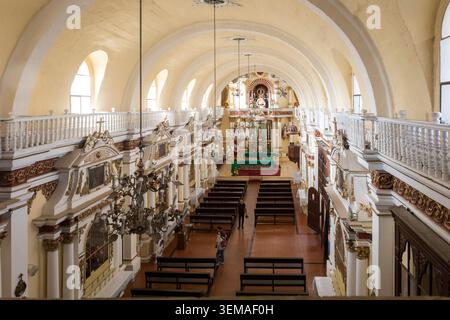 An elevated view looking down the nave of a colonial-era Catholic church in Arequipa, Peru, reveals ornate baroque altarpieces lining both sides and a Stock Photo