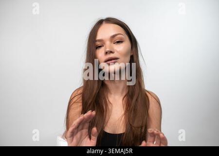 Young woman covering looking at camera and making stop gesture, posing with natural makeup and long brown hair Stock Photo