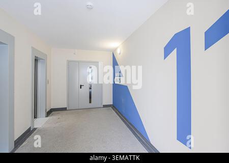 indoor shot of an apartment building corridor with an elevator and door. blue arrow points to apartments. wall has number 11 Stock Photo