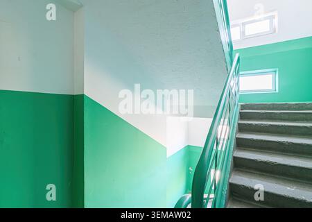 interior apartment public place, stairwell with green and white walls, concrete stairs, and a green railing. Light filters through windows. Stock Photo