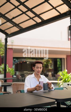 A vertical chest-up lifestyle portrait of a non-binary, gender-fluid Thai gay man from the Isan region utilizing digital technology at an outdoor terr Stock Photo