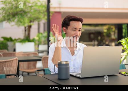 A landscape, waist-up lifestyle photograph of a non-binary, gender-fluid Thai gay man from the Isan region participating in an online business meeting Stock Photo