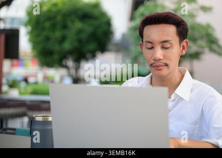 A close-up horizontal business portrait capturing a non-binary, gender-fluid Thai gay man from the Isan region deeply focused on his work. He is looki Stock Photo