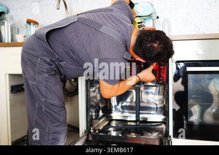 Skilled repair worker assembling a dishwasher inside kitchen cabinetry, demonstrating professional home improvement and technical expertise. Stock Photo