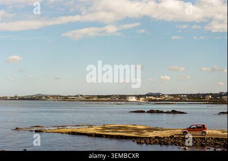 Orange Car on Jeju Coastal Pier with Calm Sea and Wide Blue Sky Stock Photo