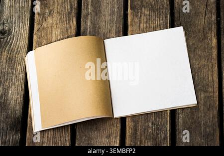 Top view of open notebook with white and kraft paper pages on a rustic wooden background. Blank book mockup with space for design. Stock Photo