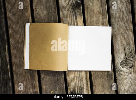 Top view of open notebook with white and kraft paper pages on a rustic wooden background. Blank book mockup with space for design. Stock Photo