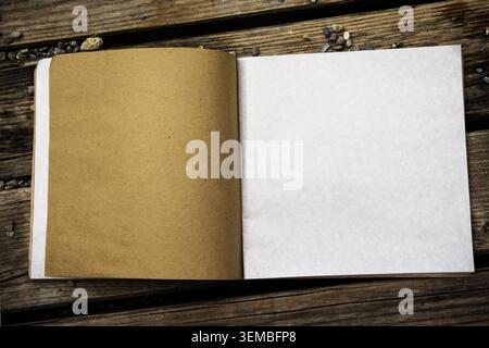 Top view of open notebook with white and kraft paper pages on a rustic wooden background. Blank book mockup with space for design. Stock Photo