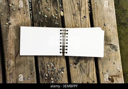 Top view of open blank white notebook on rustic wooden background with green grass. Sketchbook mockup with space for text or design. Stock Photo