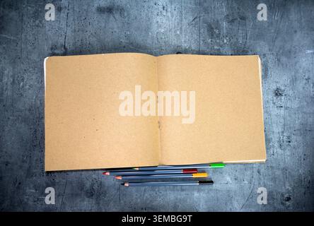 Top view of open kraft paper notebook with surrounded by pencils on a grey stone background. Stock Photo