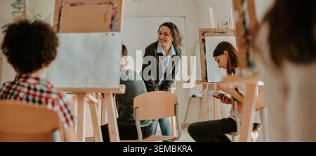 Happy Hispanic adult female teacher instructing teen students in bright art classroom Stock Photo