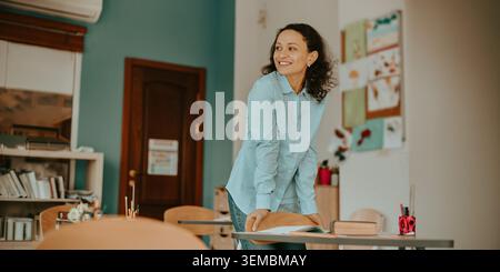 Happy Hispanic mid adult female teacher standing and smiling in a school classroom Stock Photo