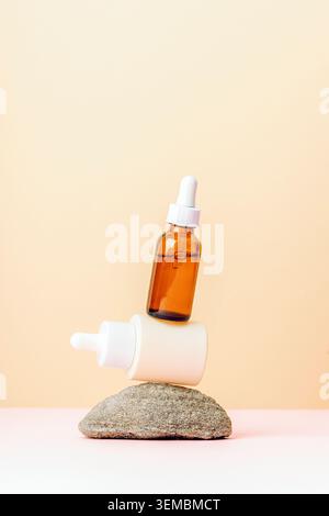 Skincare serum bottles balanced on stone against pastel background with copy space. Stock Photo