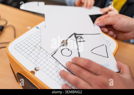 Adult and child hands working together on a white paper craft layout with a drawing over a cutting board device, creative hobby projects and early sch Stock Photo