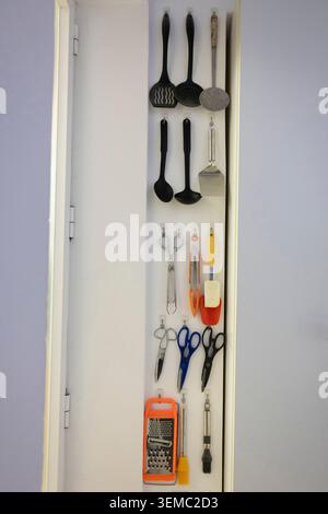 Kitchen utensils hanging on hooks providing efficient storage inside a cabinet door Stock Photo