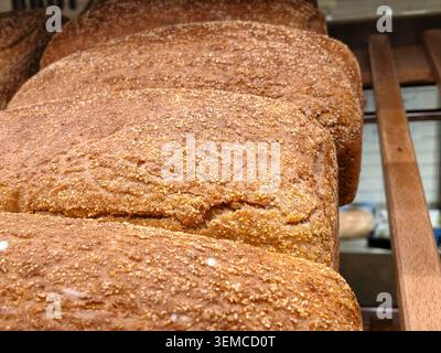 Close-up view of several crusty brown loaves arranged on a bakery rack, highlighting textured crust, grainy surface, and warm kitchen lighting that en Stock Photo