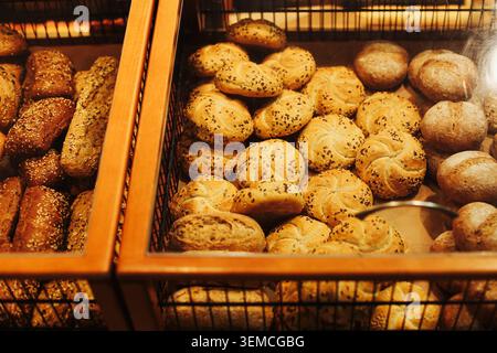 Fresh bread rolls displayed in bakery showcase. Assorted baked goods and traditional bakery products prepared for everyday meals. Stock Photo