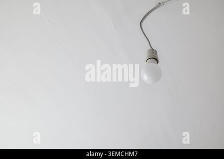 Single light bulb hanging from a wire on a white ceiling Stock Photo