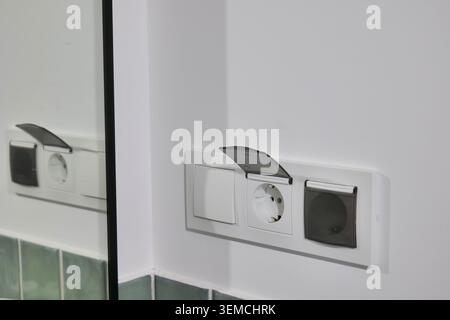 Electrical outlet and light switch on a white wall in a bathroom Stock Photo