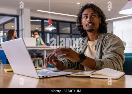 Diverse coworkers including Asian man gesturing while working on laptop at modern coworking space Stock Photo