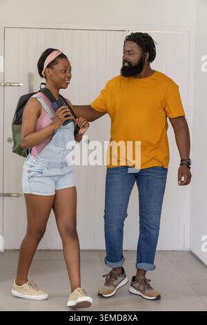 Couple with teenage woman and man standing in home entryway holding smartphone and backpack strap Stock Photo